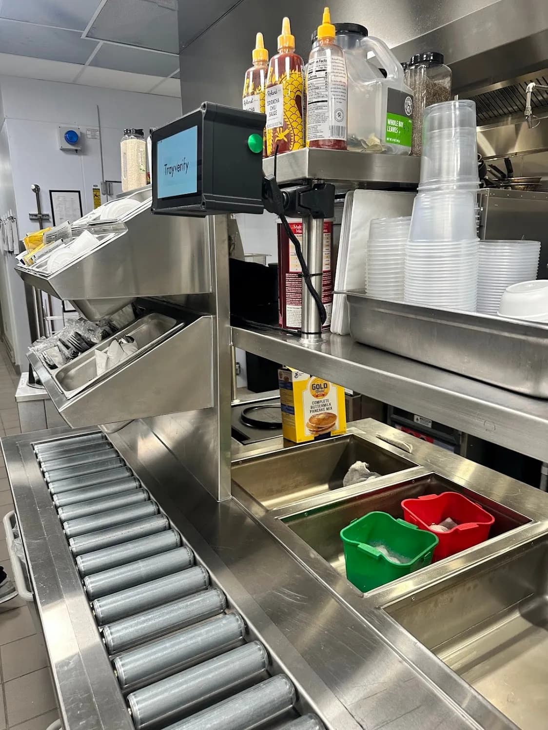 Compact TrayVerify device mounted at the end of a tray-assembly line, beside stacked cups and condiments