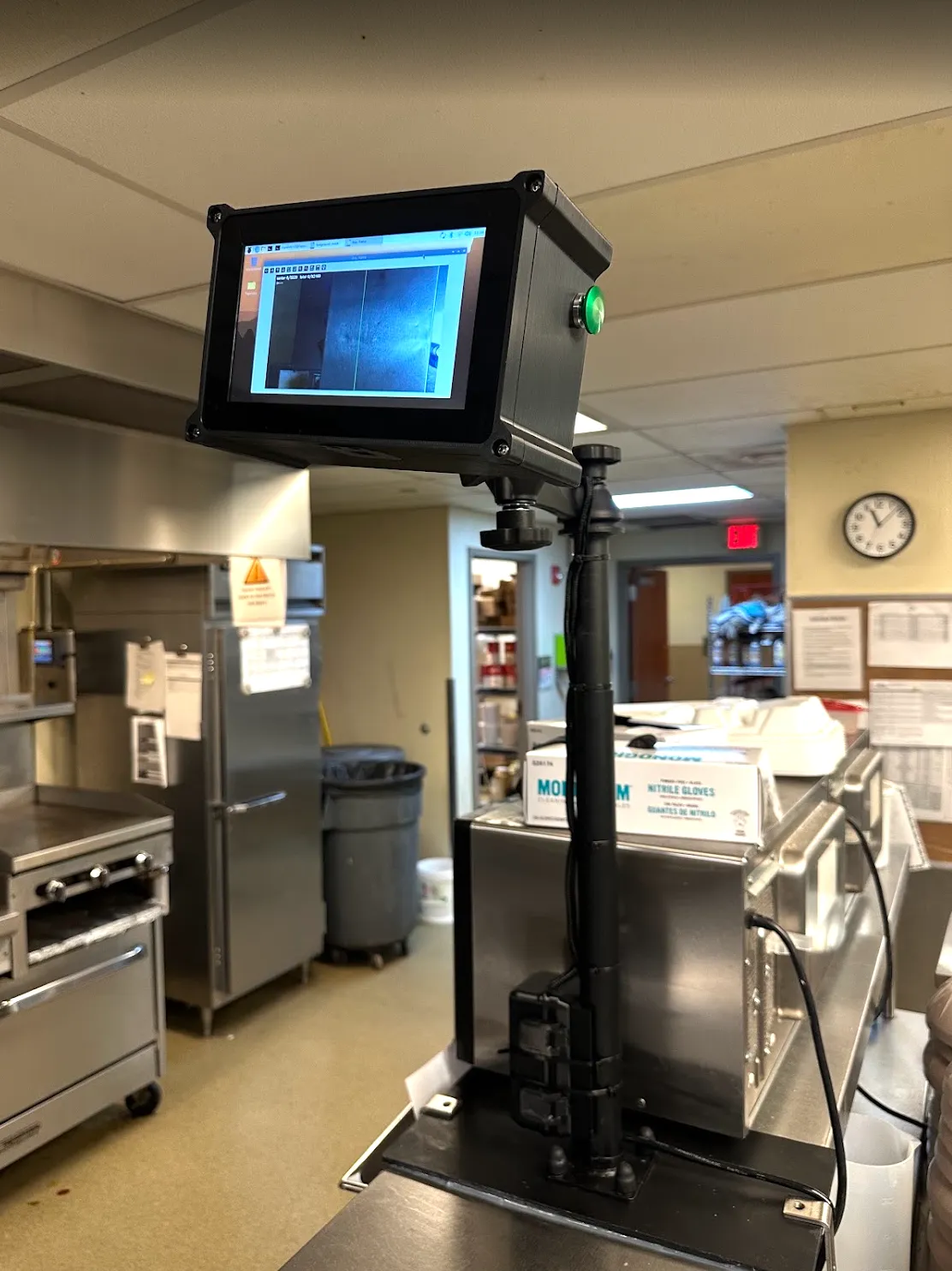 TrayVerify device on a pole mount above a stainless counter, screen showing a tray photo